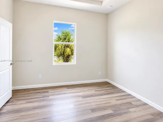 Neutral interior space featuring wood-finish flooring, recessed tray ceiling, white panel door, and a single vertical window