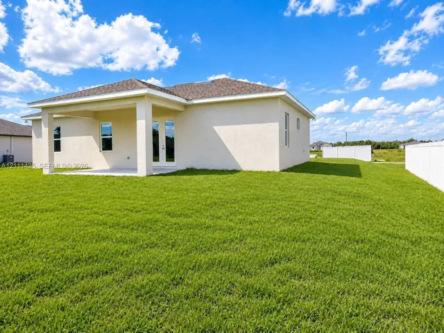 Stucco exterior featuring a covered patio, shingle roof, and expansive backyard with white privacy fencing