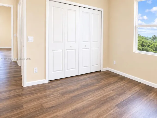 Wood-finish flooring, white paneled bi-fold closet doors, neutral wall paint, and a single-hung window