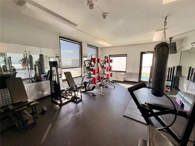 Fitness room featuring expansive mirror walls, rubberized flooring, diamond-plate metal wainscoting, and large windows