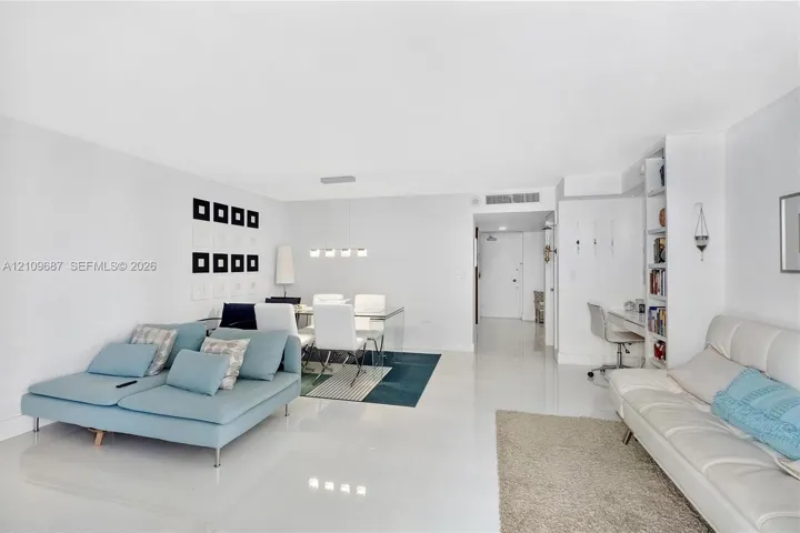 Open-concept living space featuring high-gloss tile flooring, recessed lighting, a modern multi-light linear pendant fixture, and built-in floor-to-ceiling shelving