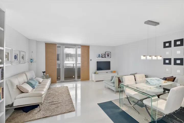 Open-concept living space featuring high-gloss tile flooring, floor-to-ceiling glass sliding doors, integrated wall shelving, and a modern multi-light linear pendant fixture