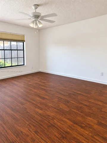 Room featuring wood-finish flooring, a multi-pane window with a neutral shade, and a white ceiling fan with integrated lighting