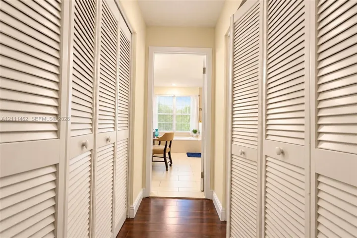 Hallway featuring full-height floor-to-ceiling louvered closet doors, wood-finish flooring, and a multi-pane window