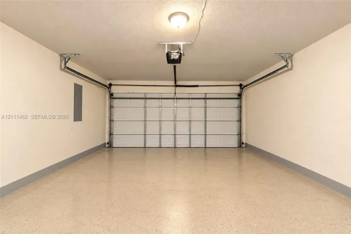 Finished garage featuring a white sectional garage door, epoxy-coated flooring, neutral wall paint, and a ceiling-mounted automatic door opener