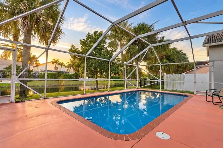 Screen-enclosed swimming pool featuring a brick-tiled perimeter and a concrete patio deck, situated on a waterfront lot with mature palm trees
