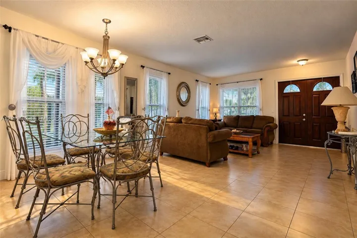 Open-concept main area featuring large-format ceramic tile flooring, double-door entry, and a multi-arm chandelier