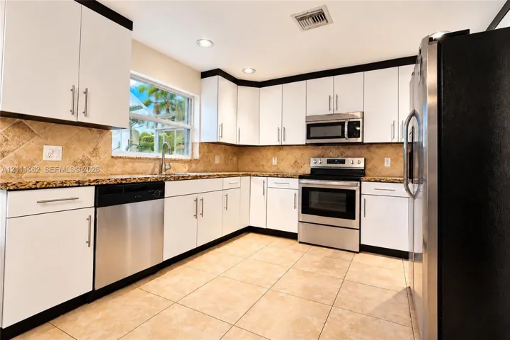 Kitchen featuring white cabinetry with dark crown molding, stone-finish countertops, tile backsplash, stainless steel appliances, and large-format floor tiling