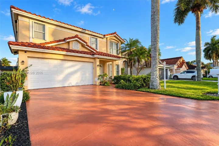 Two-story exterior featuring a clay tile roof, stucco siding, a multi-car garage, and a finished driveway