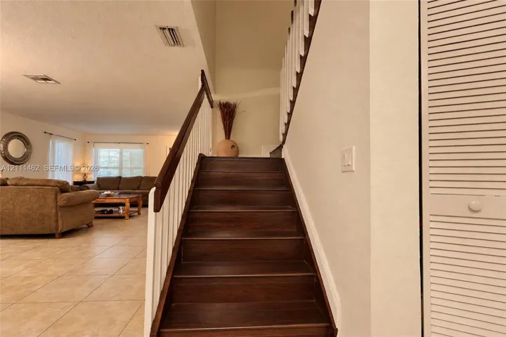 Staircase featuring dark wood-finish treads, white balusters, and a dark wood handrail, paired with neutral floor tiling and louvered closet doors