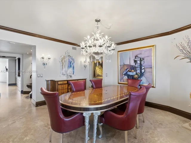 Ornate multi-tier crystal chandelier, built-in wooden sideboard with stone countertop, crown molding, stone tile flooring, and wall-mounted sconces