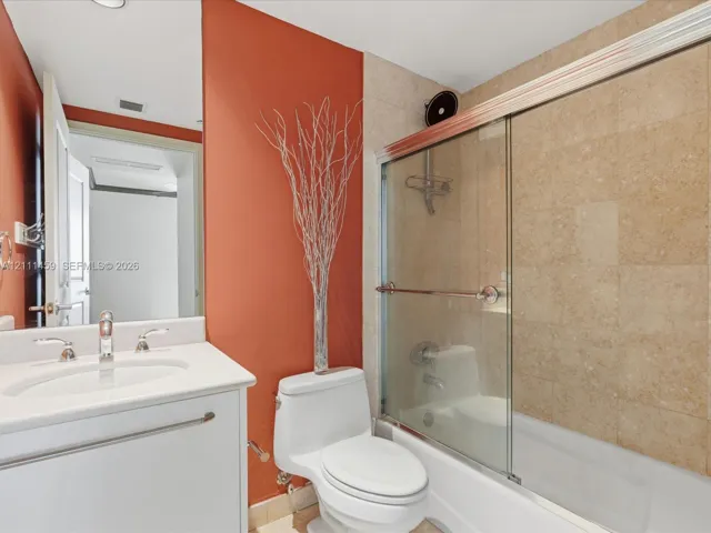 Bathroom featuring a white vanity cabinet with an integrated sink, polished metal widespread faucet, and a shower-tub combination enclosed by glass sliding doors with tiled wall surrounds
