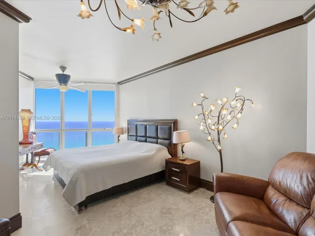 Floor-to-ceiling windows featuring ocean horizon, neutral stone flooring, decorative crown molding, and intricate multi-light chandelier