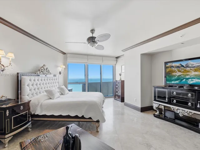 Floor-to-ceiling windows, polished stone flooring, crown molding, wall-mounted light fixtures, and a ceiling fan