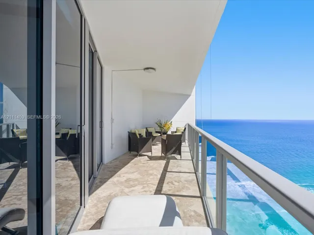 Covered balcony featuring stone-tile flooring, floor-to-ceiling glass doors, and a transparent glass railing overlooking the ocean