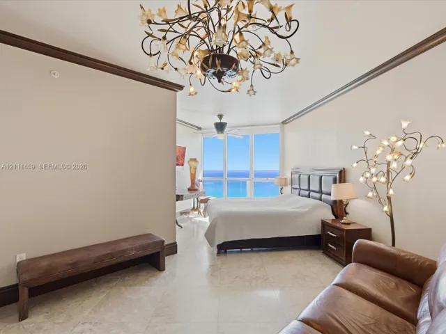 Floor-to-ceiling windows, polished stone flooring, intricate floral-style chandelier, and crown molding