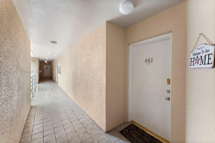Exterior hallway featuring tiled flooring, textured wall finishes, flush-mount ceiling lighting, and a metal security railing