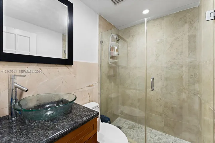 Bathroom featuring a vessel sink with a chrome faucet, stone-finish vanity countertop, large wall-mounted mirror, and a glass-enclosed shower with tiled surround