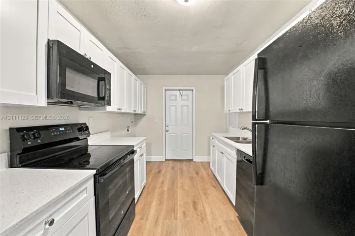 Kitchen featuring white shaker-style cabinetry, light-toned wood-finish flooring, solid surface countertops, and black built-in appliances