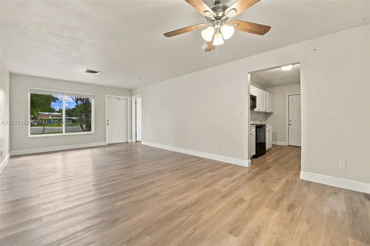 Open interior featuring wood-finish flooring, a ceiling fan with integrated lighting, and white cabinetry