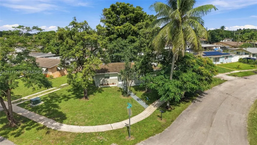 Corner lot exterior featuring established mature trees, manicured lawn, and concrete walkways