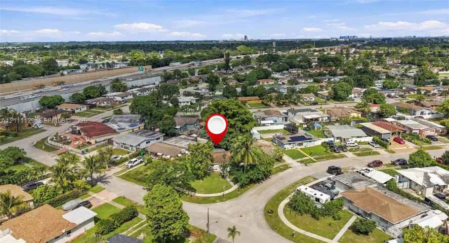 Aerial perspective of a corner lot property featuring mature shade trees, established landscaping, and paved street access within a residential neighborhood