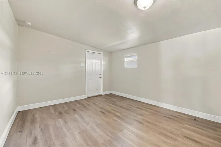 Interior space featuring wood-finish flooring, neutral wall tones, a six-panel door, and a flush-mount ceiling light fixture