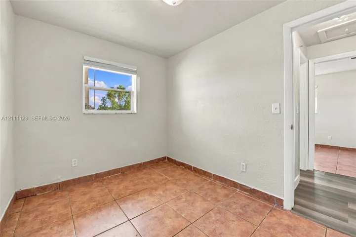 Room featuring earth-toned ceramic tile flooring, textured wall finish, and a single-pane window with horizontal blinds