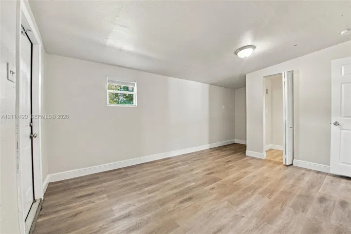 Interior space featuring light-toned wood-finish flooring, neutral wall paint, a flush-mount ceiling light, a single-pane window, and white interior doors