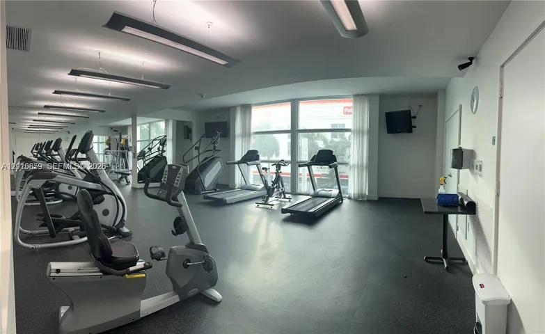 Fitness center featuring rubber flooring, floor-to-ceiling windows, wall-to-wall mirrors, and linear recessed lighting