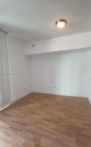 Interior room featuring wood-finish flooring, white walls, vertical blinds, and a flush-mount ceiling light fixture