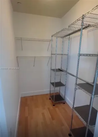 Walk-in storage space featuring wood-finish flooring and integrated metal shelving units