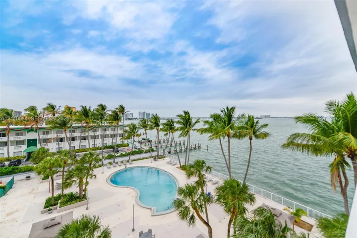 Waterfront pool deck featuring a kidney-shaped pool, paved lounging area, private dock, and mature palm trees