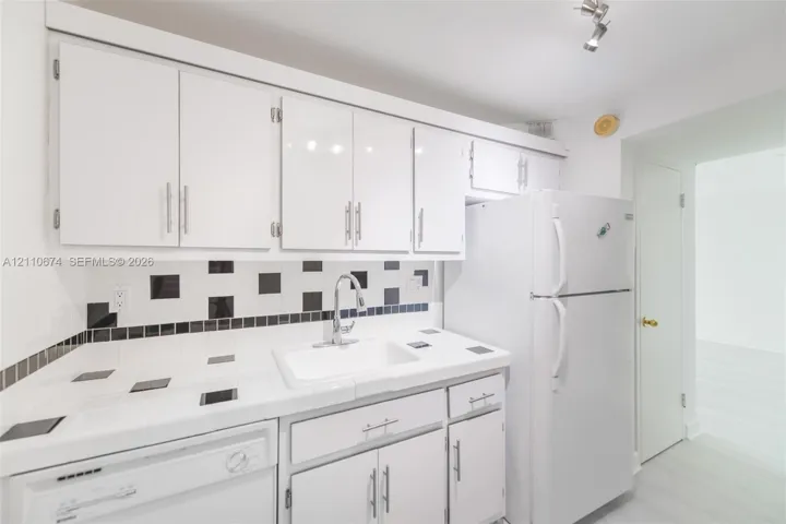 Kitchen featuring white cabinetry with metallic pulls, white tile countertops, geometric tile backsplash, undermount sink with arched faucet, and top-mount track lighting