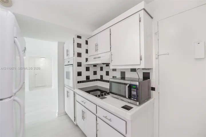 Kitchen featuring white cabinetry, a built-in oven, a black and white geometric backsplash, and light-toned flooring