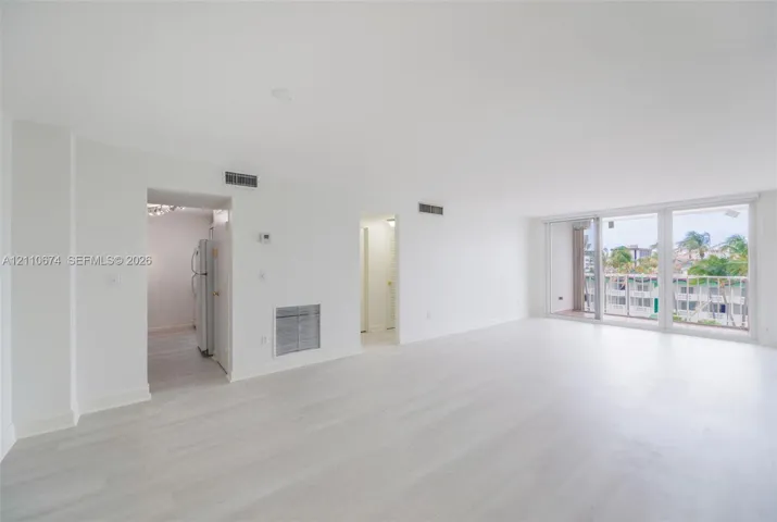 Spacious open-concept interior featuring wood-finish flooring, white walls, and floor-to-ceiling glass sliding doors leading to an exterior balcony