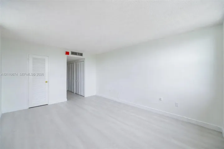 Neutral-toned room featuring wood-finish flooring, white walls, and closet doors with louvered panels