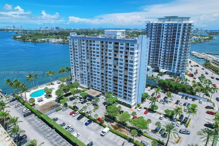 High-rise residential building featuring waterfront positioning, an outdoor swimming pool, landscaped grounds, and surface parking