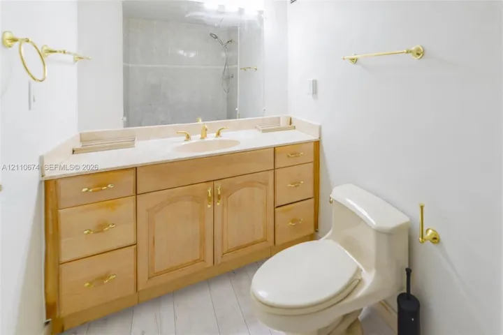 Bathroom featuring a wooden vanity with brass-finish hardware, an integrated sink with a stone countertop, a large wall-mounted mirror, and a brass-finish towel bar