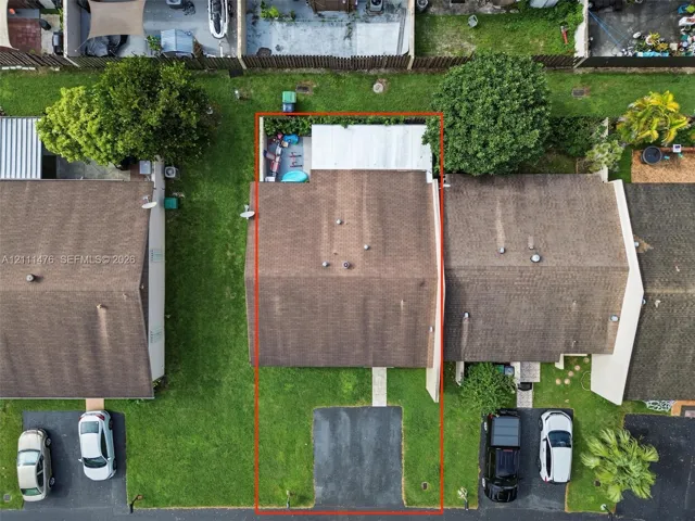 Aerial perspective featuring a shingle roof, paved driveway, concrete walkway, and private fenced rear area with a covered patio