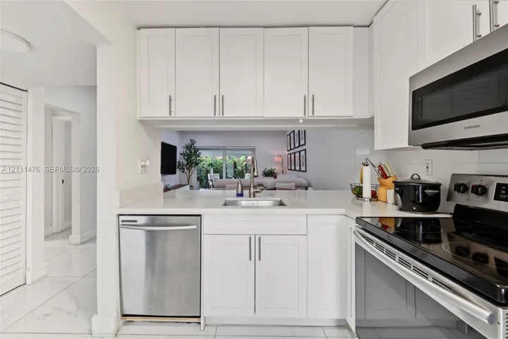 Kitchen featuring white shaker-style cabinetry, stainless steel appliances, neutral stone-finish countertops, an undermount sink, and large-format tile flooring
