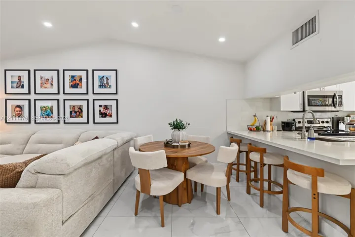 Vaulted ceilings with recessed lighting, large-format tile flooring, and kitchen peninsula featuring a stone countertop and undermount sink