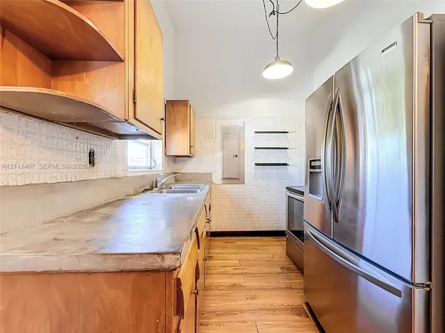 Kitchen featuring wood-finish cabinetry, solid surface countertops, a stainless steel refrigerator, textured wall tile, and wood-finish flooring