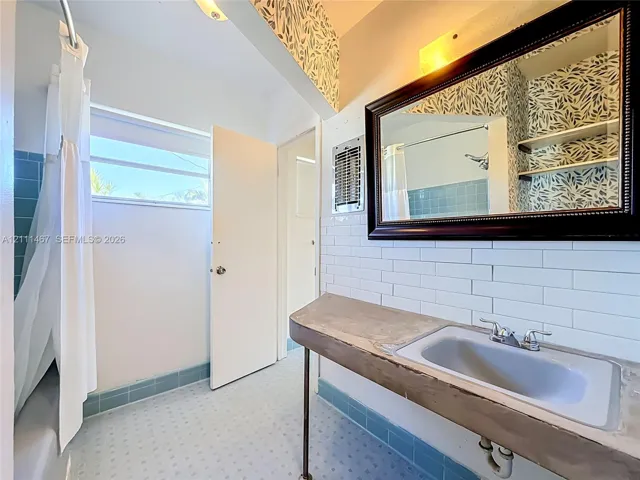 Bathroom featuring a wall-mounted sink with a concrete-finish countertop, white subway tile backsplash, blue ceramic wall and floor tile, and a framed vanity mirror