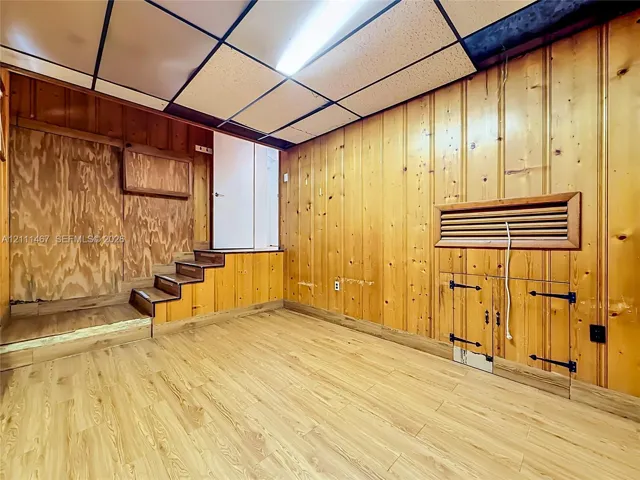 Interior space featuring natural wood wall paneling, wood-finish flooring, built-in storage cabinetry with iron hardware, and a drop ceiling with integrated lighting