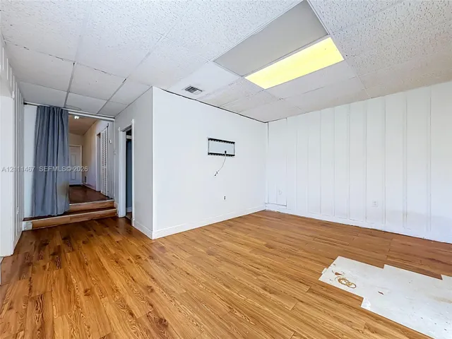 Interior space featuring wood-finish flooring, vertical panel wall detailing, and a drop ceiling with integrated fluorescent lighting