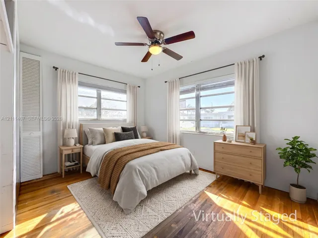 Bedroom featuring wood-finish flooring, dual windows with blinds, a ceiling fan with light fixture, and floor-to-ceiling louvered closet doors