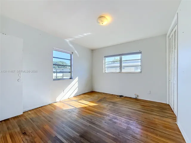 Interior space featuring wood-finish flooring, two horizontal-pane windows, and a built-in closet with louvered doors