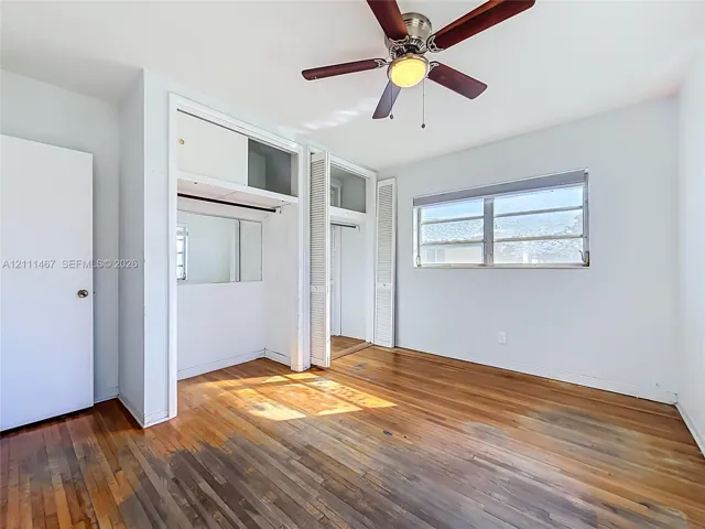 Wood-finish flooring, ceiling fan with integrated lighting, and built-in closet storage featuring mirrored panels