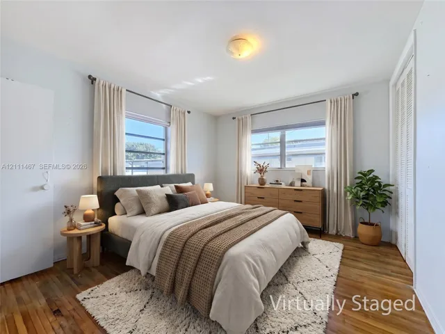 Bedroom featuring wood-finish flooring, dual windows, and louvered-door closets